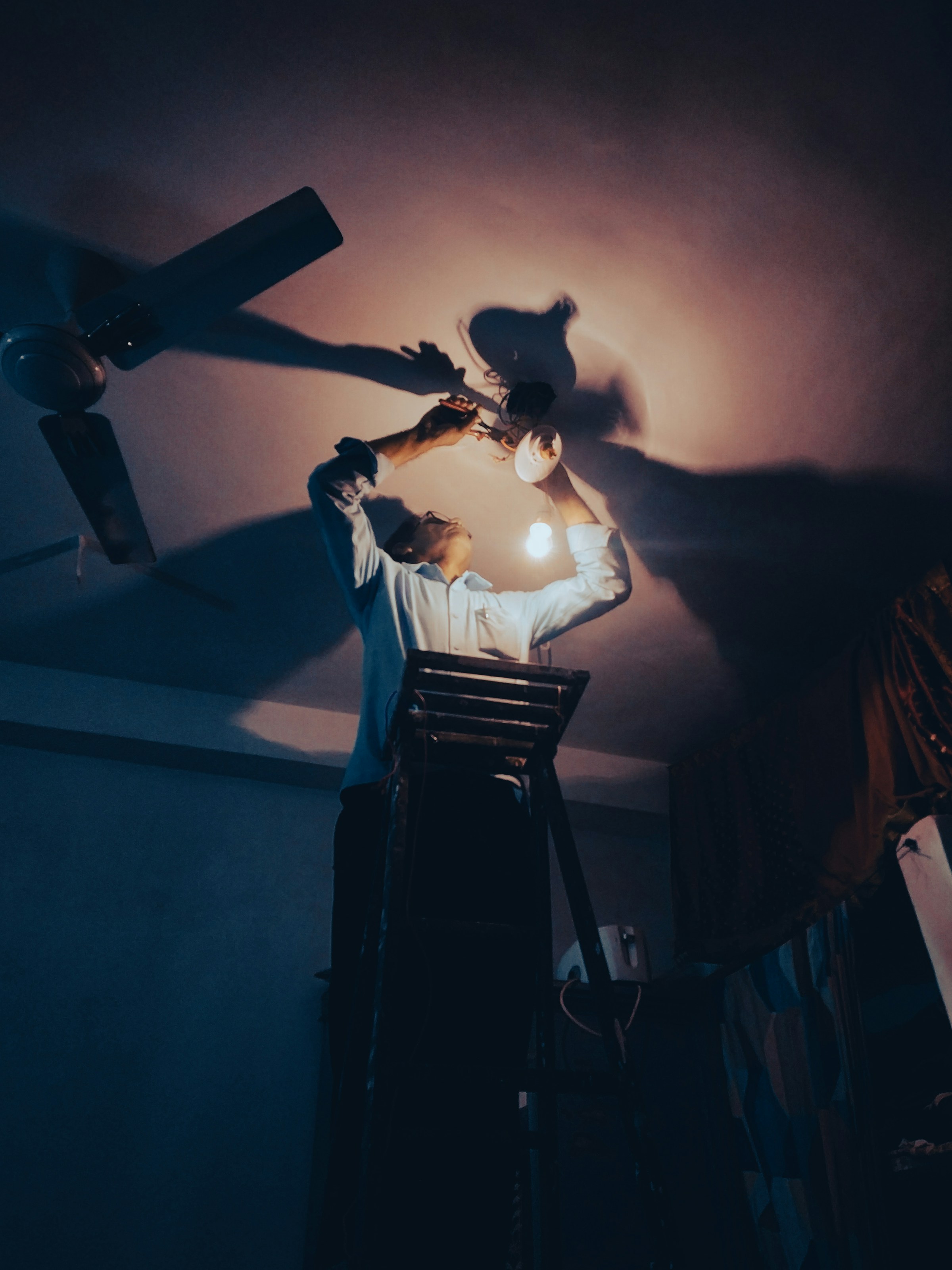 A technician working late at night, fixing a light fixture by hand